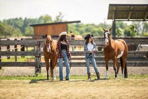 Two young cowgirls walk their paint horses on a ranch in the summer photo