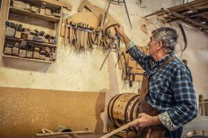 más viejo artesano escoge necesario partes para haciendo de madera productos en un rústico taller foto