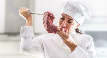 Female chef in rondon smells fresh cut of red meat with pleasure photo