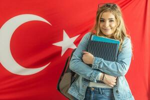 Beautiful student girl smiles holding study materials with a flag of Turkey behind her photo