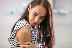 Female who just got vaccinated against Covid-19 looks at her arm with a plaster on it photo