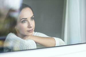 Loneliness impact of a quarantine during pandemic makes sad woman look out from the window photo