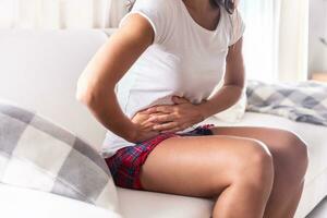 Woman sitting on a couch at home holding her appendix in a stomach ache photo