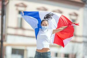 hembra en un cara máscara sostiene un francés bandera en el calle, celebrando un victoria foto