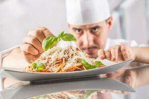 Chef in restaurant kitchen prepares and decorates meal with hands.Cook preparing spaghetti bolognese photo