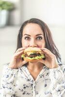 Young woman holding a burger in front of her mouth photo