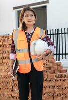 civil Ingenieria mujer en pie a moderno el construcción sitio vistiendo naranja la seguridad chaleco participación tableta tecnología y casco,inspectores para cheque liza detalles edificio proyecto industria . foto