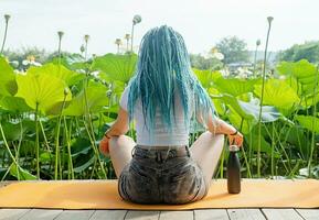 joven mujer con hermosa azul rastas descansando en yoga estera en loto lago foto