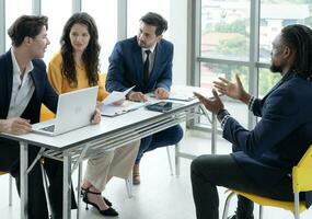 Job interview concept. Employer and diverse hr team doing job interview with a black man in business office. Job candidate talks with human resources team. Hiring, employment, and recruitment concept. photo