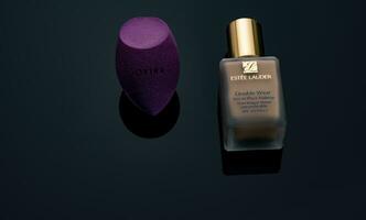 CHONBURI, THAILAND-DECEMBER 15, 2022 Jovina makeup sponge and Estee Lauder makeup foundation bottle on dark background. Liquid beige make-up foundation and beauty blender on black background. photo