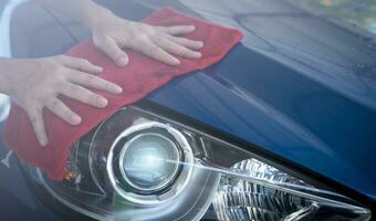 Car wash service. Man hand holding red microfiber cloth and polish headlight of blue car. Auto care service business concept. Man cleaning and detailing luxury car. Clean water drops from luxury car. photo