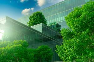 Eco-friendly building with vertical garden in modern city. Green tree forest on sustainable glass building. Energy-saving architecture with vertical garden. Office building with green environment. photo