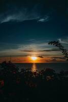 Bright orange sunset on the dark Indian Ocean on Bali island. Evening sunlight, fire sky, amazing view with flowers photo