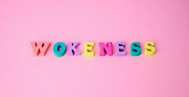 the word wokeness laid with colorful wooden letters against pink background photo