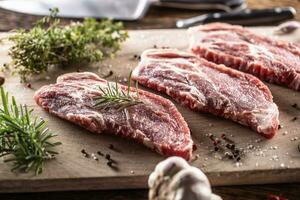 Raw pork neck cut on a cutting board with rosemary and thyme herbs photo