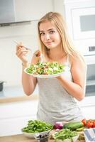 Young happy blonde girl eating healthy salad from arugula spinach tomatoes olives onion and olive oil photo