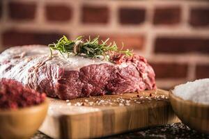 Raw beef ribe-eye steak with salt pepper and herbs on wooden butcher board photo