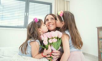 contento de la madre día concepto. pequeño hijas Gemelos Beso su madre con un tulipán ramo de flores foto