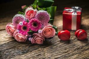 Beautiful bouquet of flowers with red gift and hearts on wooden table. photo