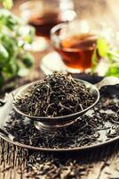 Dried tea leaves in bowl on rustic wooden table photo