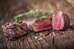 Grilled beef steak with rosemary, salt and pepper on old cutting board. Beef tenderloin steak. photo