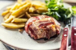 Camambert cheese wrapped in bacon slices and fried, served with chips and green salad. photo