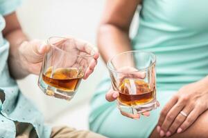 Man and woman hands toasting with glasses of whiskey brandy or rum indoors - closeup photo