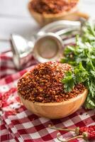 Dried and crushed chili peppers in wooden bowles with parsley herbs photo