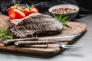 Two beef rump steaks with herbs tomatoes salt and spices on butcher board photo