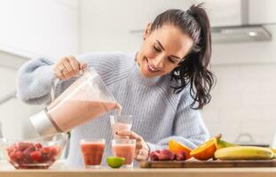 Woman pours fruit smoothie into cups in a kitchen photo