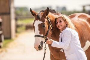 Vet leans towards the brown paint horse holding it by the bridle, smiling photo