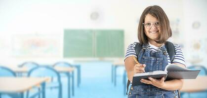 Young student writes down notes into a notebook by a pencil while standing with a backpack on isolated background photo