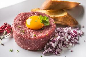 Beef tartare with egg yolk red onion chili peppers herbs and bruschetta photo