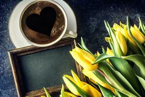 Top of view cup form coffee with heart empty chalkboard and spring tulips on wooden table photo