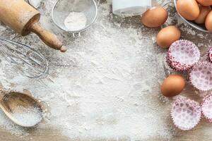 Baking utensils with eggs flour and cupcake cases on kitchen table - Top of view photo