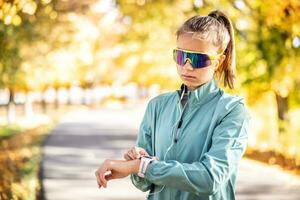 mujer deportivo al aire libre usa auriculares y mira a el relojes inteligentes en su muñeca foto