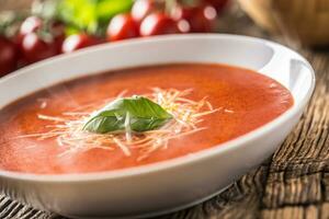 Hot tomato soup parmesan cheese and basil leave on old oal table photo