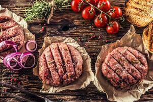 crudo hamburguesas en de madera mesa con cebolla Tomates hierbas y especias foto