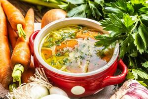 Chicken soup broth in a vintage bowl with homemade noodles carrot onion celery herbs garlic and fresh vegetables photo