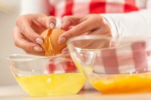 Detail of woman's hands separating egg yolks from the whites into two glass bowls photo