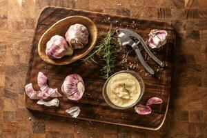 Top view of a vintage board with garlic heads, cloves, paste, a crusher, salt and rosemary photo