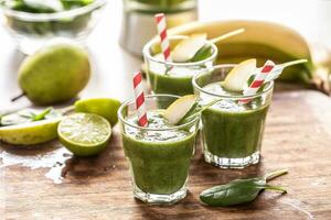 Cups of green smoothie with colorful paper straws and wedges of lime on a table photo