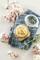 Top view aromatic garlic paste in a glass jar laid on rustic kitchen cloth with bulbs and peeled cloves and rosemary photo