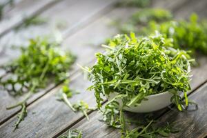 Fresh arugula salad in white dish on wooden table photo