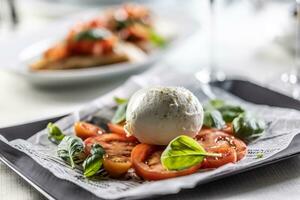 Caprese style salad with sliced tomatoes, basil and ball of buffalo mozzarella. photo