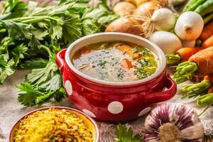 Chicken soup broth in a vintage bowl with homemade noodles carrot onion celery herbs garlic and fresh vegetables photo