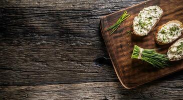 Banner of bread slices with a dairy product spread, freshly cut chives placed on a dark brown cutting board and vintage background photo