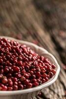 Red peppercorn in bowl on oak table photo