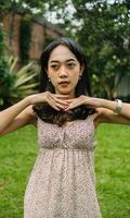 an Asian woman in a patterned dress posing with her hands in a garden photo