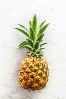 Fresh whole pineapple with leaves on a marble surface photo